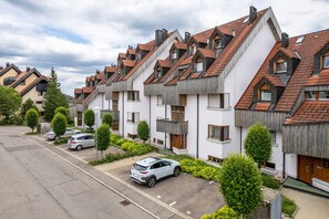 Une rangée d’immeubles résidentiels modernes, dotés de toits inclinés et de balcons, un parking et des espaces verts aménagés.