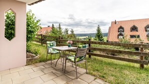 Une terrasse extérieure avec une table et des chaises, une clôture en bois et une vue sur des maisons et de la verdure.