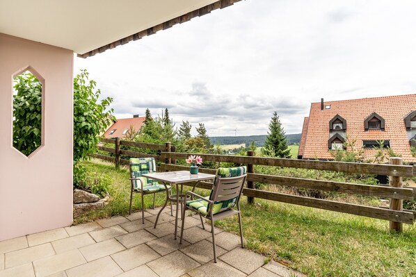 Une terrasse extérieure avec une table et des chaises, une clôture en bois et une vue sur des maisons et de la verdure.
