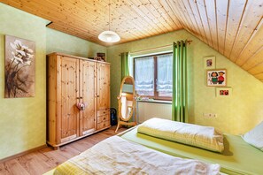 Une chambre avec deux lits, une armoire en bois, un radiateur, une fenêtre avec des rideaux et un ventilateur de plafond.