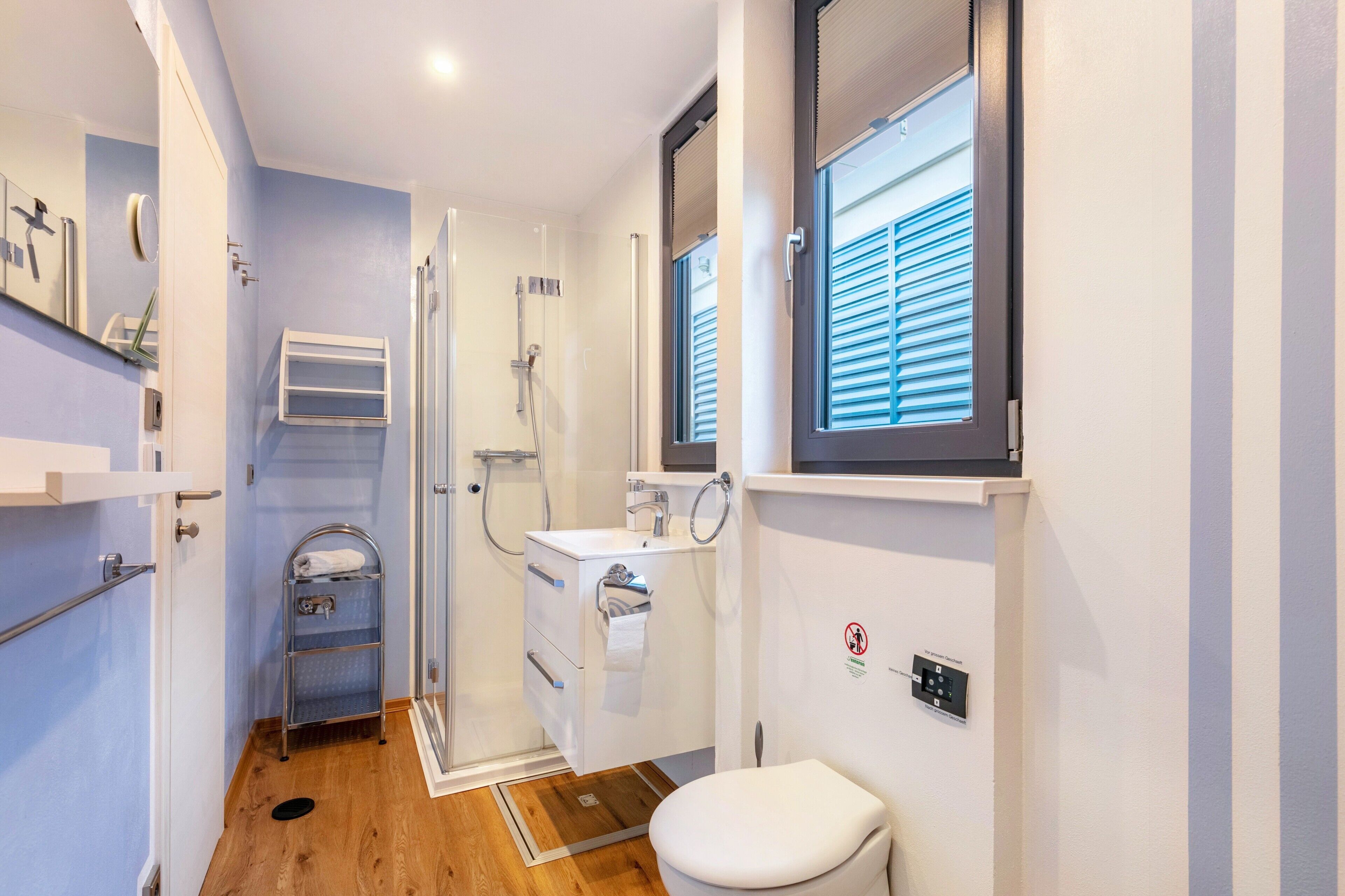 Une petite salle de bain comprenant une douche, des toilettes et un lavabo, avec un plancher en bois et des murs bleu clair.