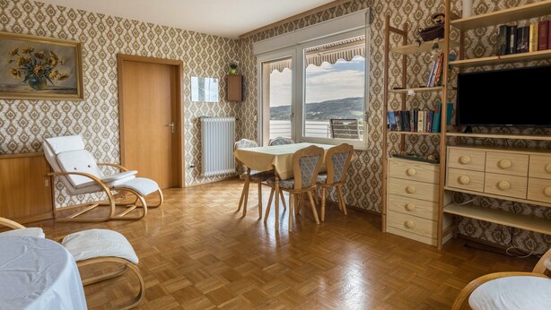 Una stanza con pavimento in legno, un tavolo da pranzo con sedie, una libreria, una televisione e una finestra con vista.