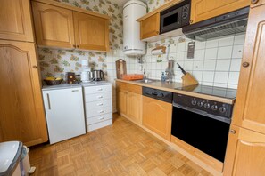 A kitchen with wooden cabinets, a white refrigerator, a stove, and a microwave. - Apartment 'See- Panorama' with Lake View, Balcony and Wi-Fi (Gaienhofen)