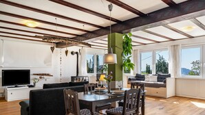 A modern living room with a wooden floor, a dining table with chairs, a sofa, a TV, and large windows. - Apartment 'Augensteins Burgzimmer' with Private Terrace and Wi-Fi (Seelbach)