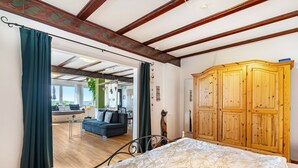 A bedroom with a bed, wooden wardrobe, and a view of a living room with a sofa and curtains. - Apartment 'Augensteins Burgzimmer' with Private Terrace and Wi-Fi (Seelbach)