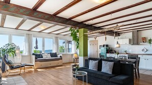 A spacious living area with a wooden floor, a dark grey sofa, a small round table, and a kitchen in the background. - Apartment 'Augensteins Burgzimmer' with Private Terrace and Wi-Fi (Seelbach)