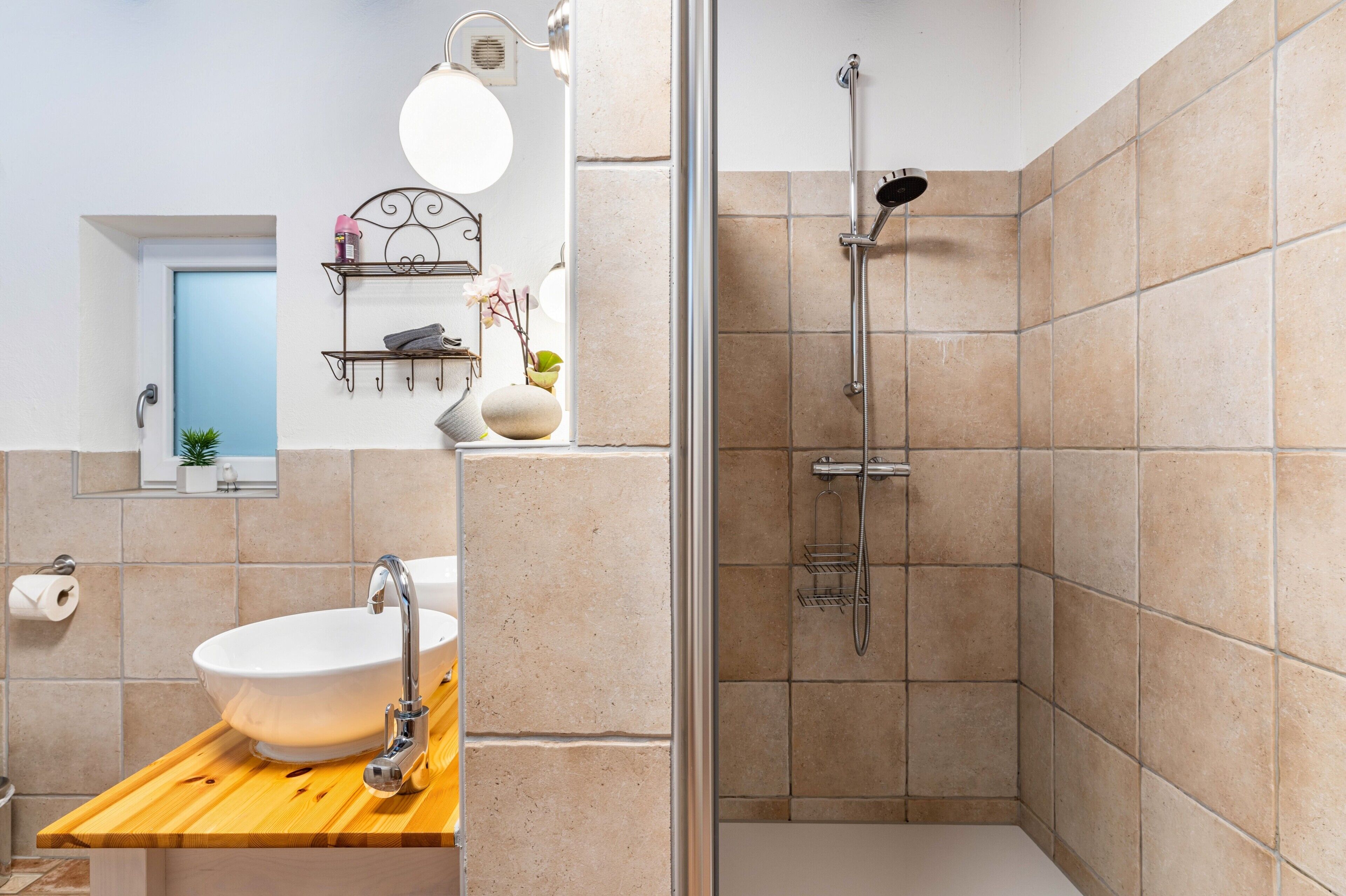A bathroom with a freestanding bathtub, a sink with a wooden countertop, a shower with a handheld showerhead, and a mirror with a wall-mounted light fixture.