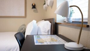 Une chambre d’hôtel avec un lit, un bureau avec une carte, une lampe et une fenêtre avec des stores.