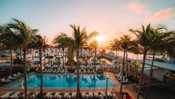 Zwembadgedeelte van een resort met ligbedden en palmbomen, omringd door resortgebouwen.