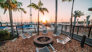 Vuurkorf omringd door stoelen op een terras met grind, met uitzicht op een jachthaven op de achtergrond.