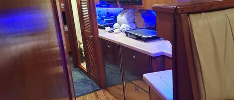 Un pasillo estrecho revestido de madera, con una zona de kitchenette que incluye un microondas, una computadora portátil y algunos alimentos.
