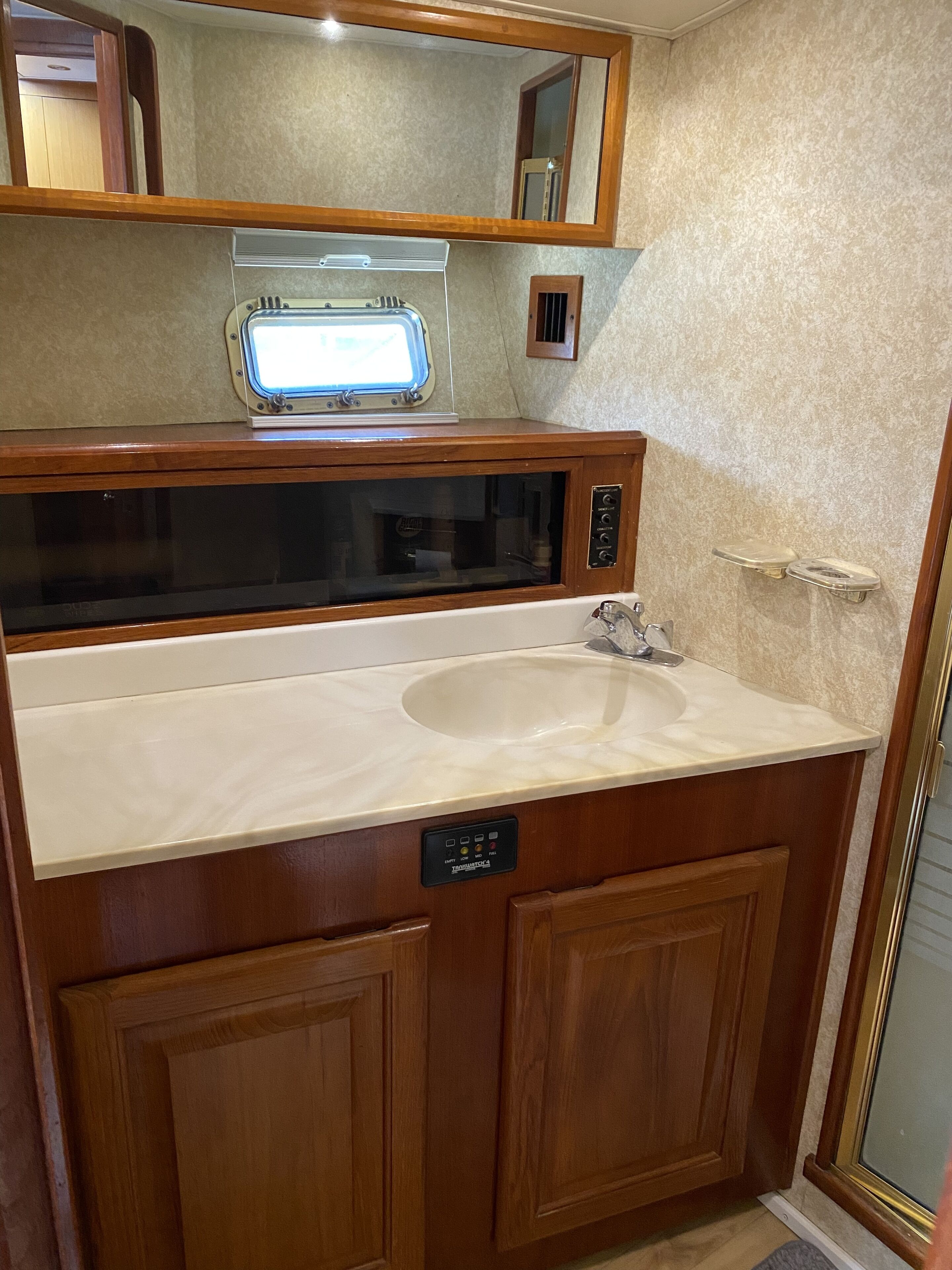 A bathroom with a wooden vanity, a built-in microwave, and a large mirror above the sink.