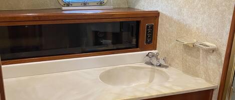 A bathroom with a wooden vanity, a built-in microwave, and a large mirror above the sink.