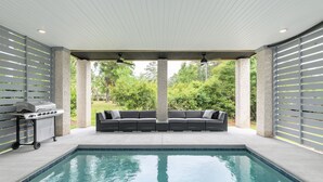 Zona de piscina al aire libre con área de estar integrada, una parrilla y vistas de la vegetación circundante.