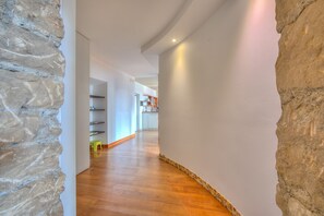 A hallway with stone walls, wooden flooring, and a view into a kitchen area.