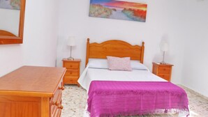 A bedroom with a wooden bed, a nightstand with a lamp, a dresser, and a painting on the wall. - Chalet Blue in Conil de la Frontera (Conil de la Frontera)