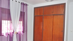 A room with a large wooden wardrobe, a window with purple curtains, and a tiled floor. - Chalet Blue in Conil de la Frontera (Conil de la Frontera)