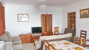 A living room with a sofa, a television, a cabinet, and a dining table with chairs. - Chalet Blue in Conil de la Frontera (Conil de la Frontera)