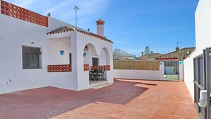 A courtyard with a tiled floor, a white building with a tiled roof, and a small patio area with a table and chairs. - Chalet Blue in Conil de la Frontera (Conil de la Frontera)