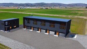Un edificio moderno con techo plano y ventanas amplias, rodeado de campos abiertos y colinas lejanas.