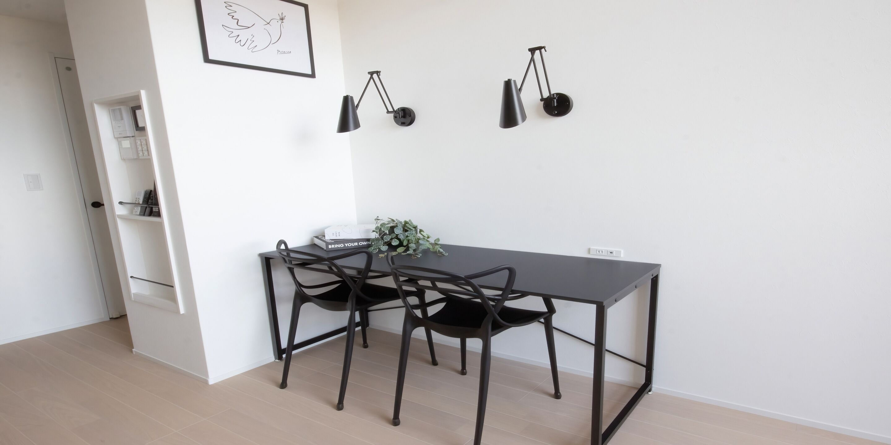 A minimalist dining area with a dark table, two chairs, and a wall-mounted lamp.