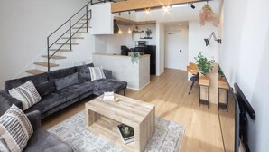 Una sala de estar moderna con un sofá gris, una mesa de centro de madera y una escalera que conduce a un nivel superior.