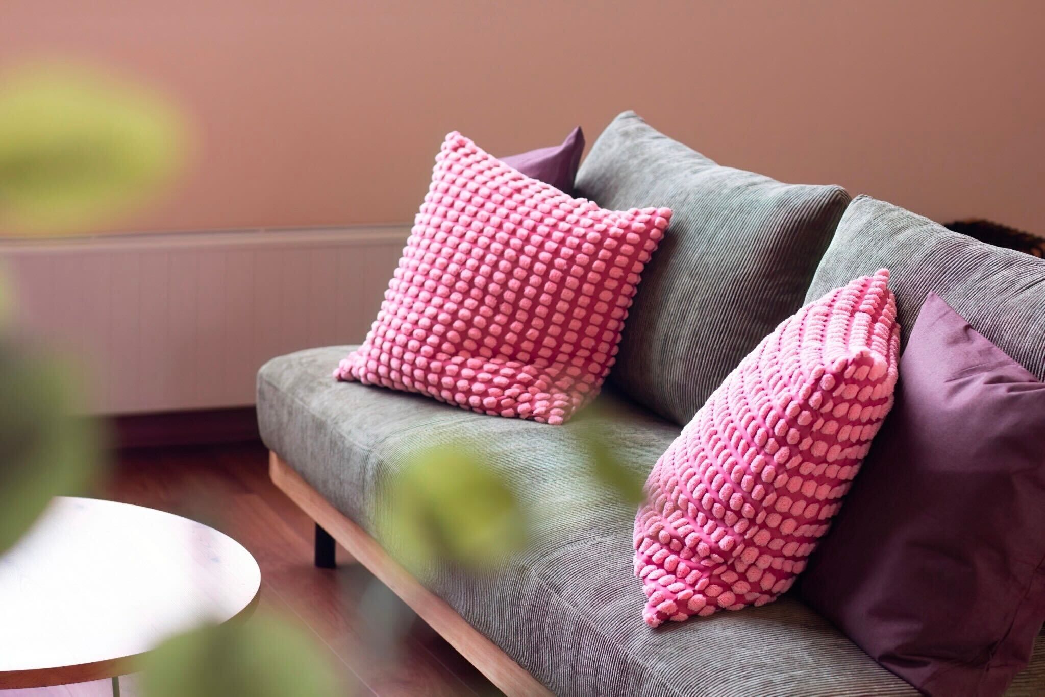 A grey sofa with pink and purple cushions.