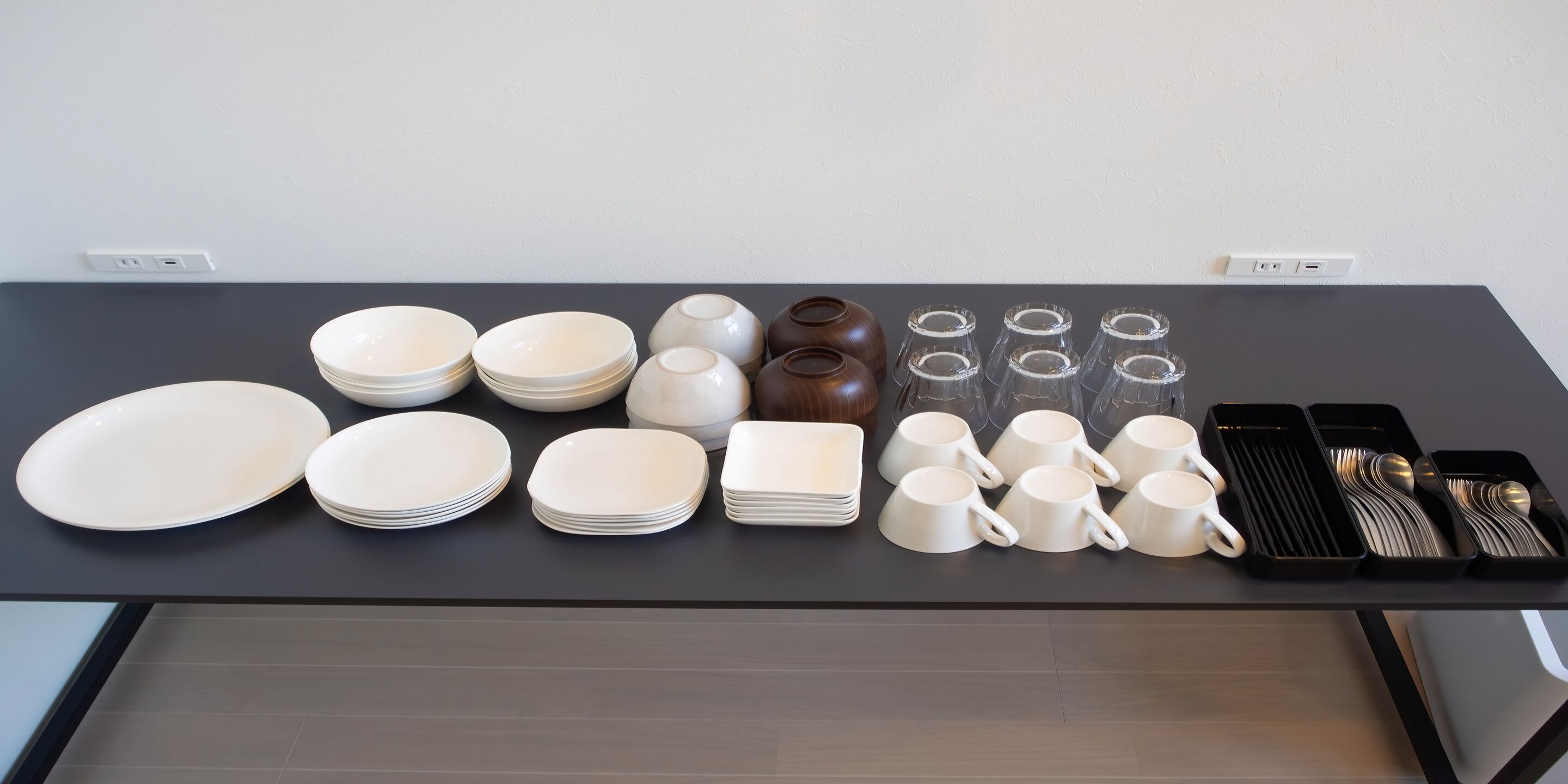 Une table bien dressée, avec différents éléments de service, notamment des assiettes, des bols, des tasses et des couverts.