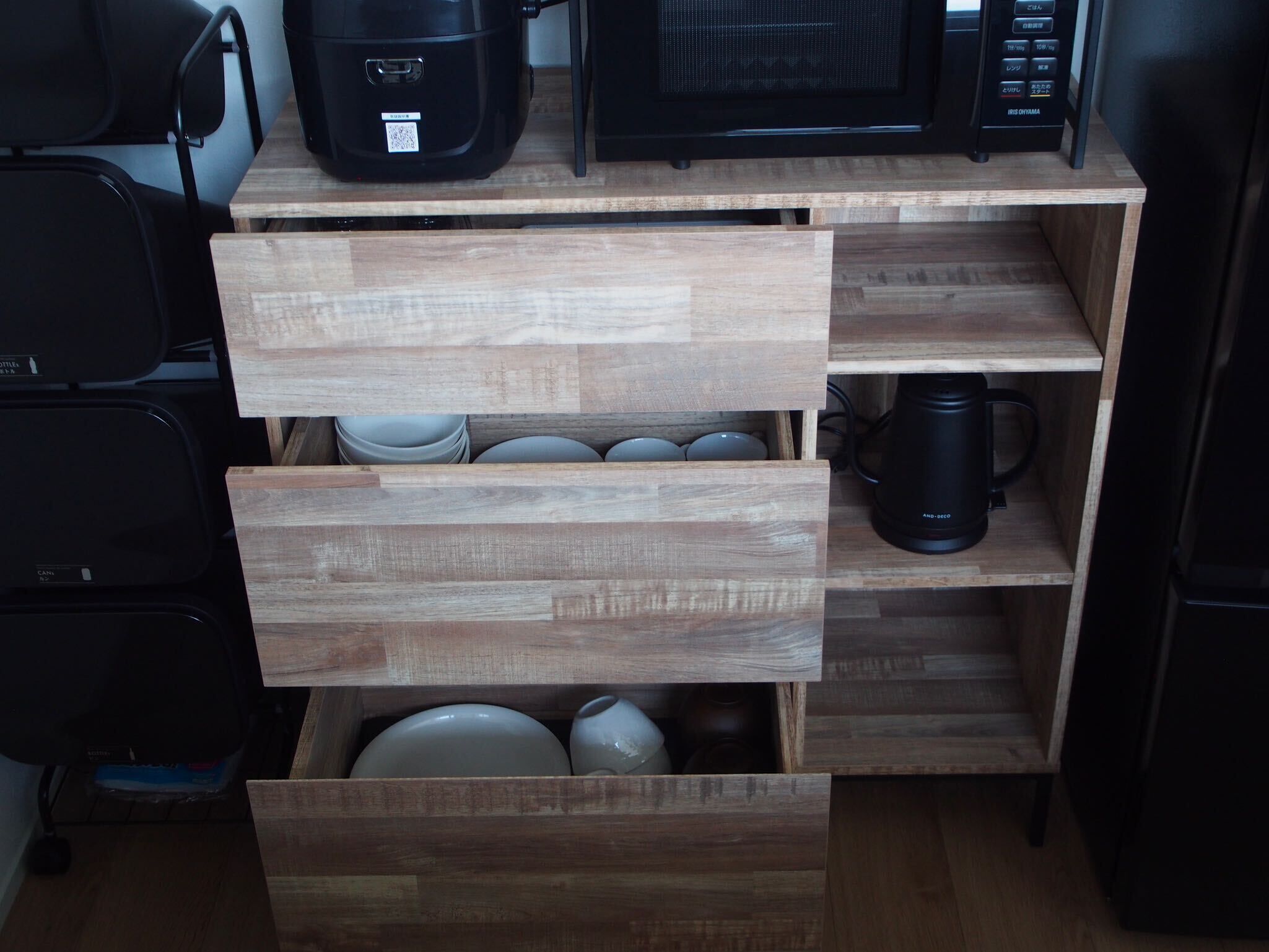 A compact kitchen with wooden cabinetry, a microwave, a coffee maker, and a rice cooker.