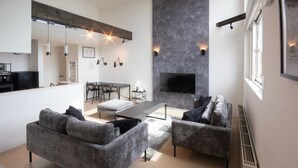 Una sala de estar moderna con sofás grises, una mesa de comedor y un televisor de pantalla plana montado en una pared con textura.