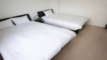 Twee eenpersoonsbedden met witte beddengoed en zwarte hoofdborden in een kamer met licht houten vloeren en een potplant.