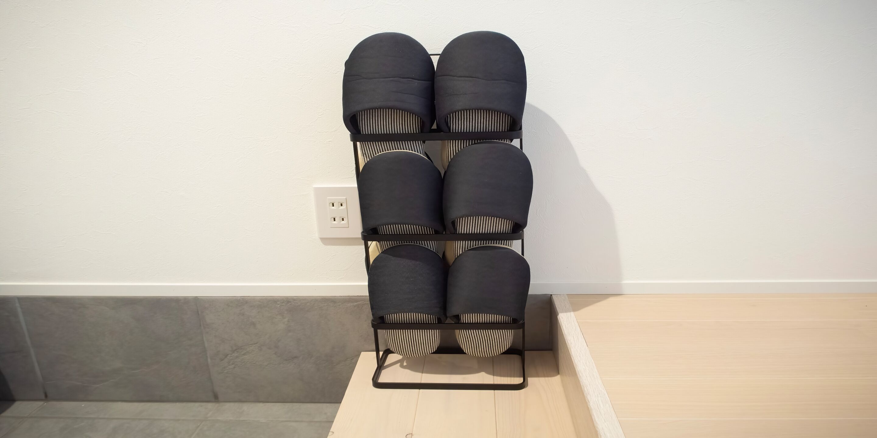 A black shoe rack with six pairs of shoes against a white wall.