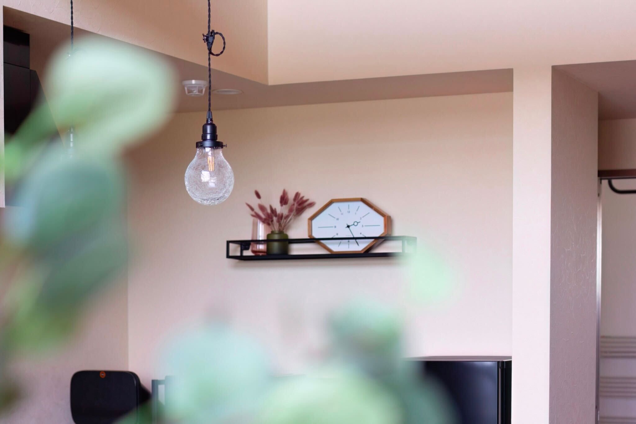 A modern living room with a hanging light fixture, a clock, and a shelf with decorative items.