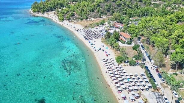 A coastal area with a beach, clear turquoise waters, and a line of parked cars along the shore. - Spacious Maisonette on the "eu Blue Beach" of Kalogria in Sithonia in Greece (Sithonia)