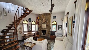 A cozy living room with a stone floor, a wooden staircase, a fireplace, and a sofa. - Spacious Maisonette on the "eu Blue Beach" of Kalogria in Sithonia in Greece (Sithonia)