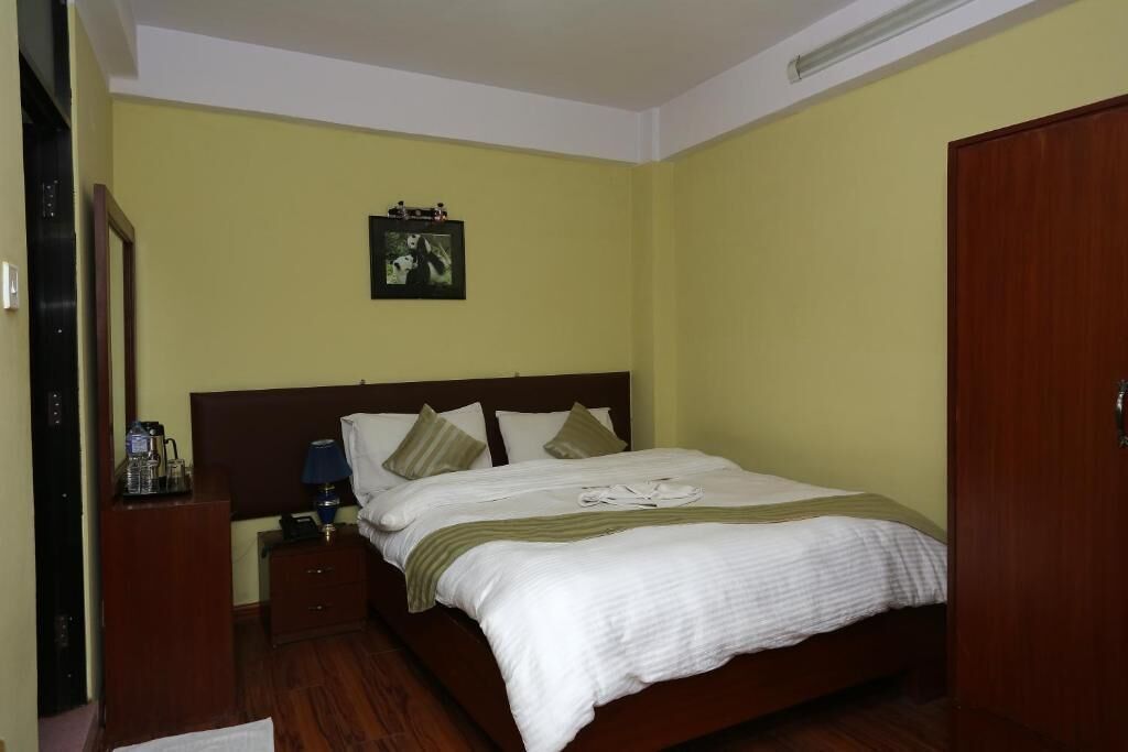 Una cama individual con cabecera de madera, una mesita de noche con lámpara, y un cuadro en la pared.
