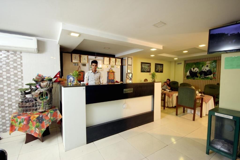 A hotel reception area with a reception desk, a TV mounted on the wall, and a panda mural.