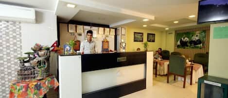 A hotel reception area with a reception desk, a TV mounted on the wall, and a panda mural.