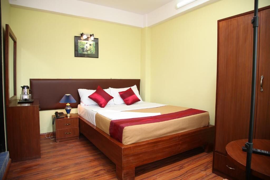 A hotel room with a wooden bed, a nightstand, a lamp, a wardrobe, and a framed picture on the wall.