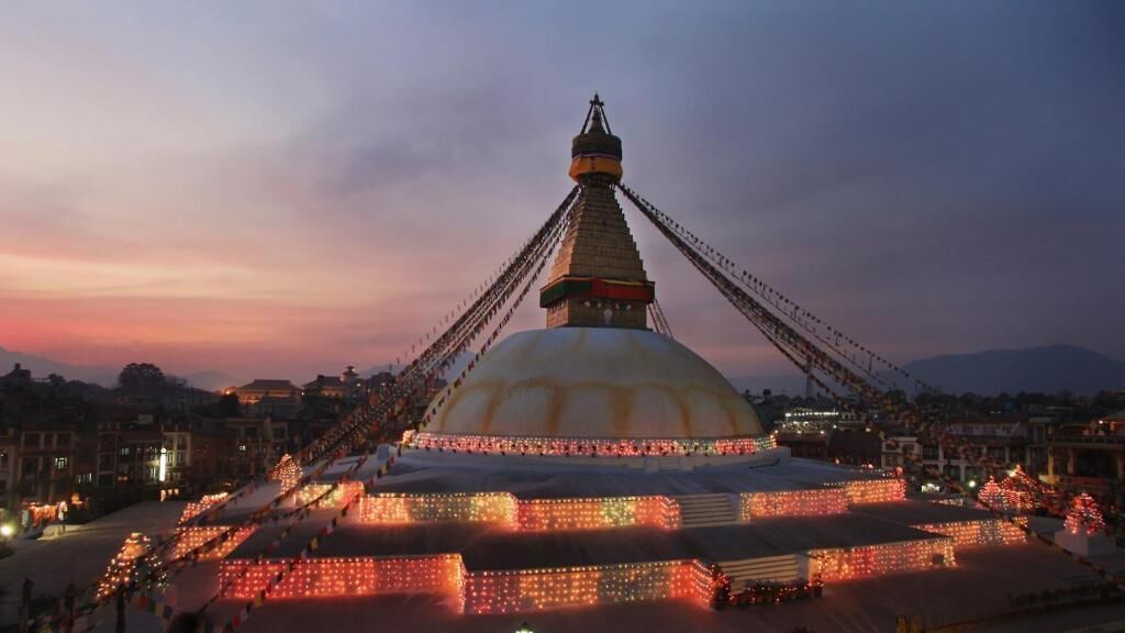 A large, illuminated stupa with a prominent central spire, surrounded by a well-lit area with visible steps leading up to it.