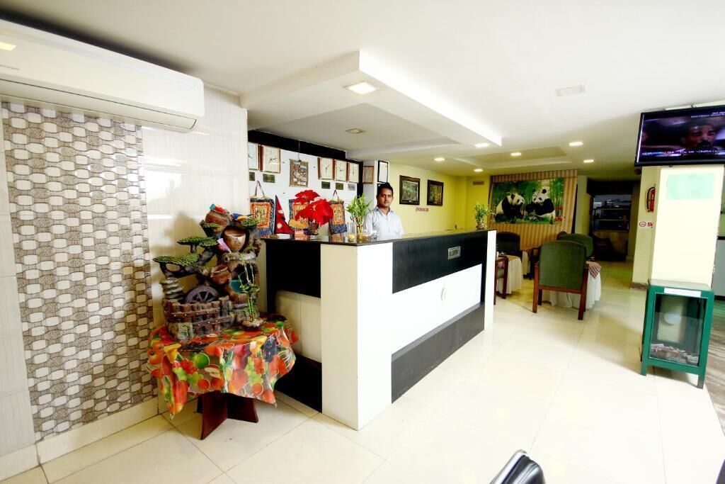 A hotel reception area with a counter, a small table with decorative items, and a television screen.