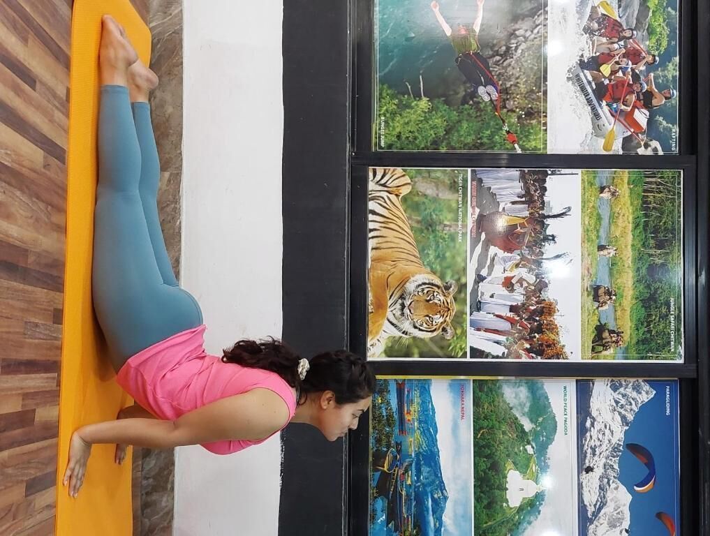 A person performing a yoga pose on a mat in front of a wall with framed pictures.
