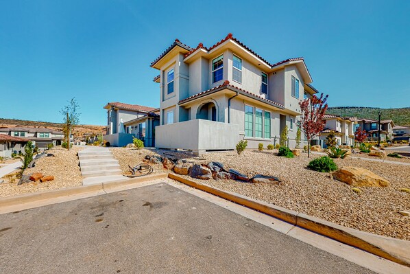 A two-story house with a tiled roof, a driveway, and a landscaped garden with rocks and small plants.