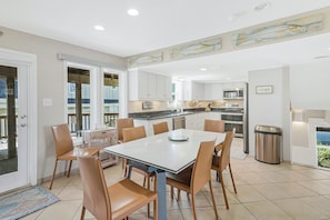 Une cuisine moderne avec des armoires blanches, un évier en acier inoxydable et un coin repas comprenant une table blanche et des chaises marron.
