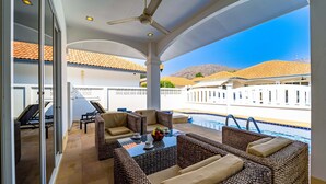 Un patio soleado con mobiliario de mimbre, una piscina y vistas a edificios al fondo.