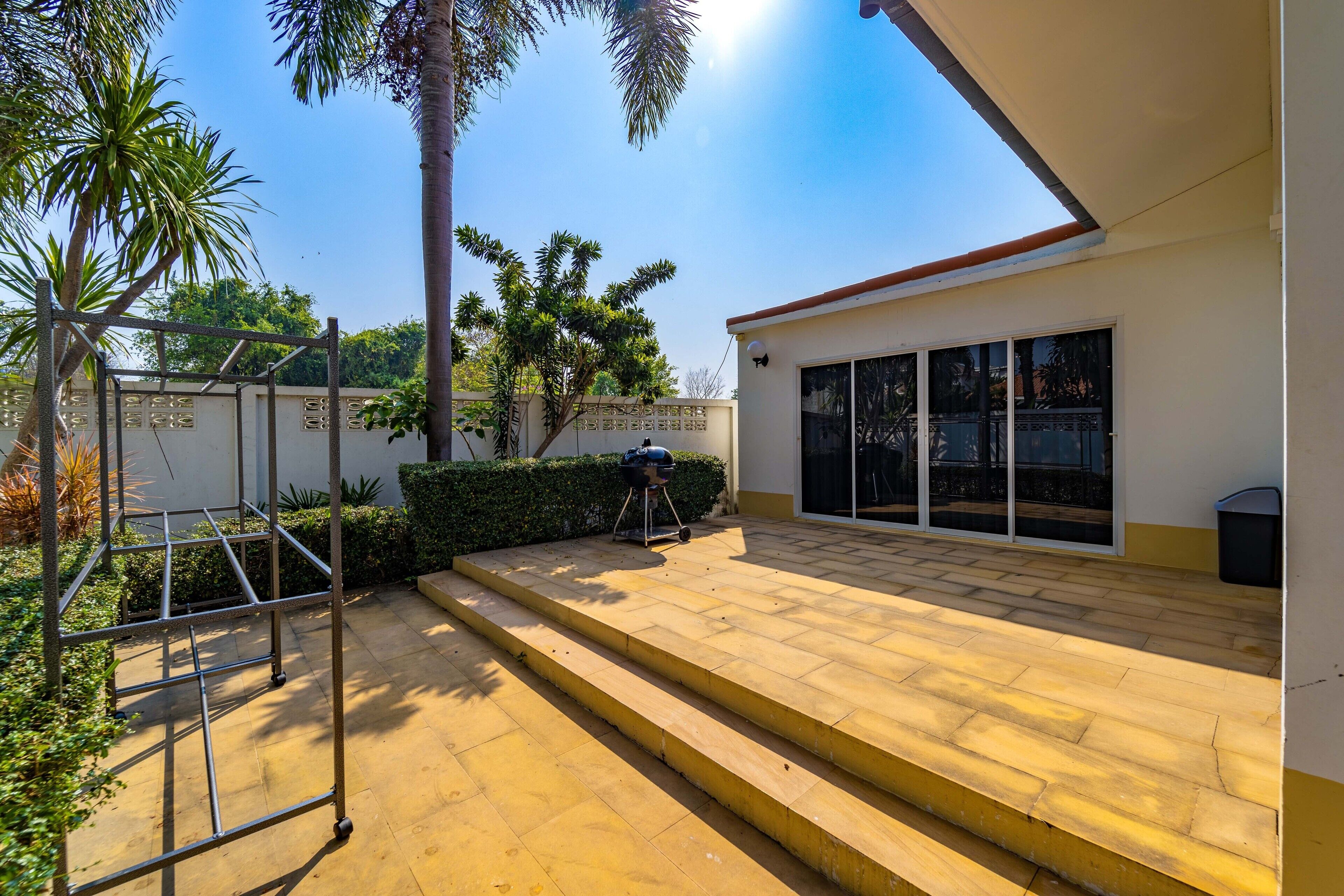 Eine Terrasse mit Metallgestell, einem Grill und einer Treppe zu einem überdachten Bereich mit einer Glastür.