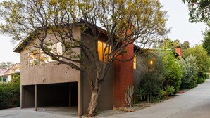 Une maison moderne avec un garage, un arbre devant et un jardin bien entretenu.
