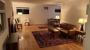 Un salon avec un canapé en cuir marron, une table basse et une table à manger avec des chaises. Deux lampes sont posées sur des tables d’appoint.