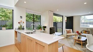 Una cocina moderna con una isla central, un comedor con mesa y sillas, y vistas al exterior a través de amplios ventanales.