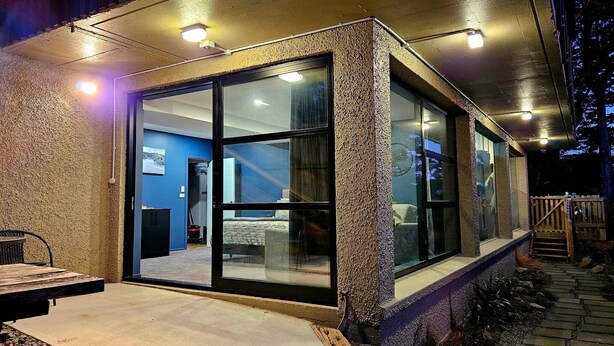 Una casa moderna amb una porta de vidre que dona a un saló, façana de pedra i una petita zona d'estar a l'exterior.